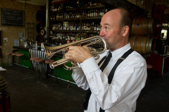 David playing cornet in front of a wall of bottles and barrels