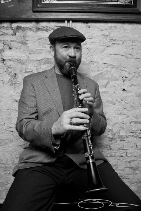 David Jellema playing clarinet against a whitewashed brick wall